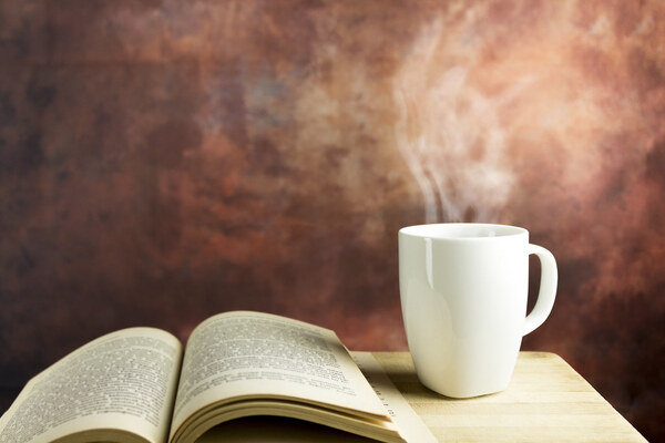 Open book on a wooden table with a cup of coffee